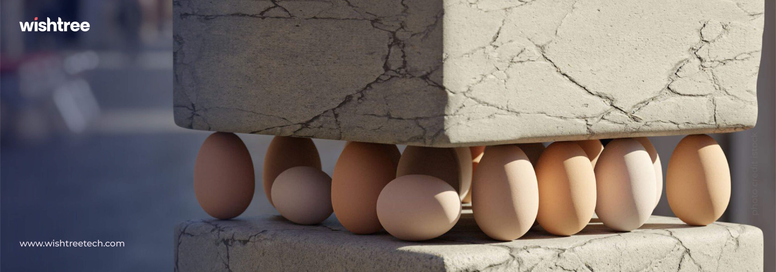 A low-angle shot shows several brown and white eggs supporting a large, rough concrete block that rests on another concrete block. The concrete has visible cracks and a textured surface. The scene illustrates fragility supporting immense weight. The "wishtree" logo is in the top left corner, and a website URL is in the bottom left.
