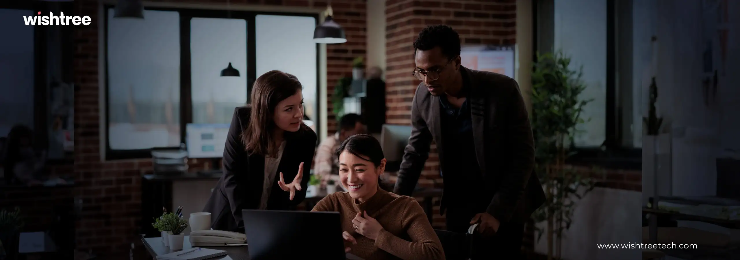 Diverse team collaborating and discussing work around a laptop in an office.