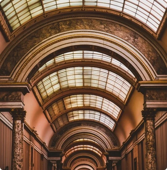 A view of an ornate hallway with arched, glass-paneled ceilings, marble columns, and decorative architectural details.