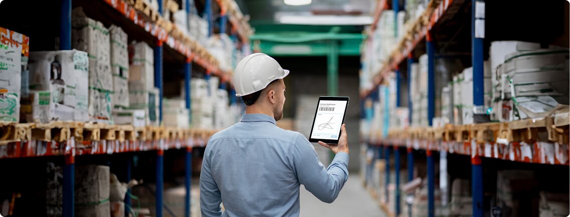 Warehouse employee wearing a hard hat and holding a tablet displaying inventory data, symbolizing Unified Commerce Transformation and digital inventory management for a distributor.